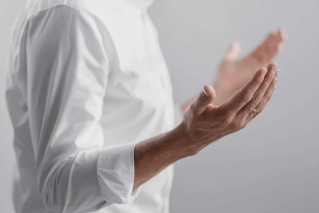 man in white t-shirt praying with his hands wide open 