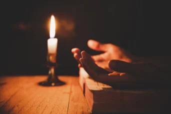 man praying with bible and lit candle