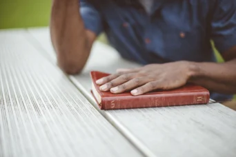 male hand on bible wooden table