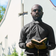 priest standing near the church with a bible