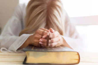 woman praying on bible with cross in her hands