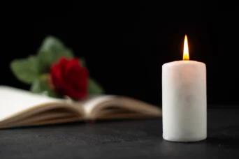 burning candle with a red rose and book laying on the table