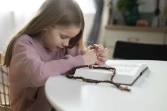 A little girl is praying by the table with her hands on the Bible
